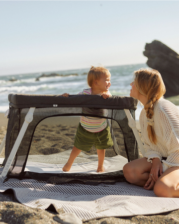 A young child playing in the Lotus Travel Crib while set up on a beach